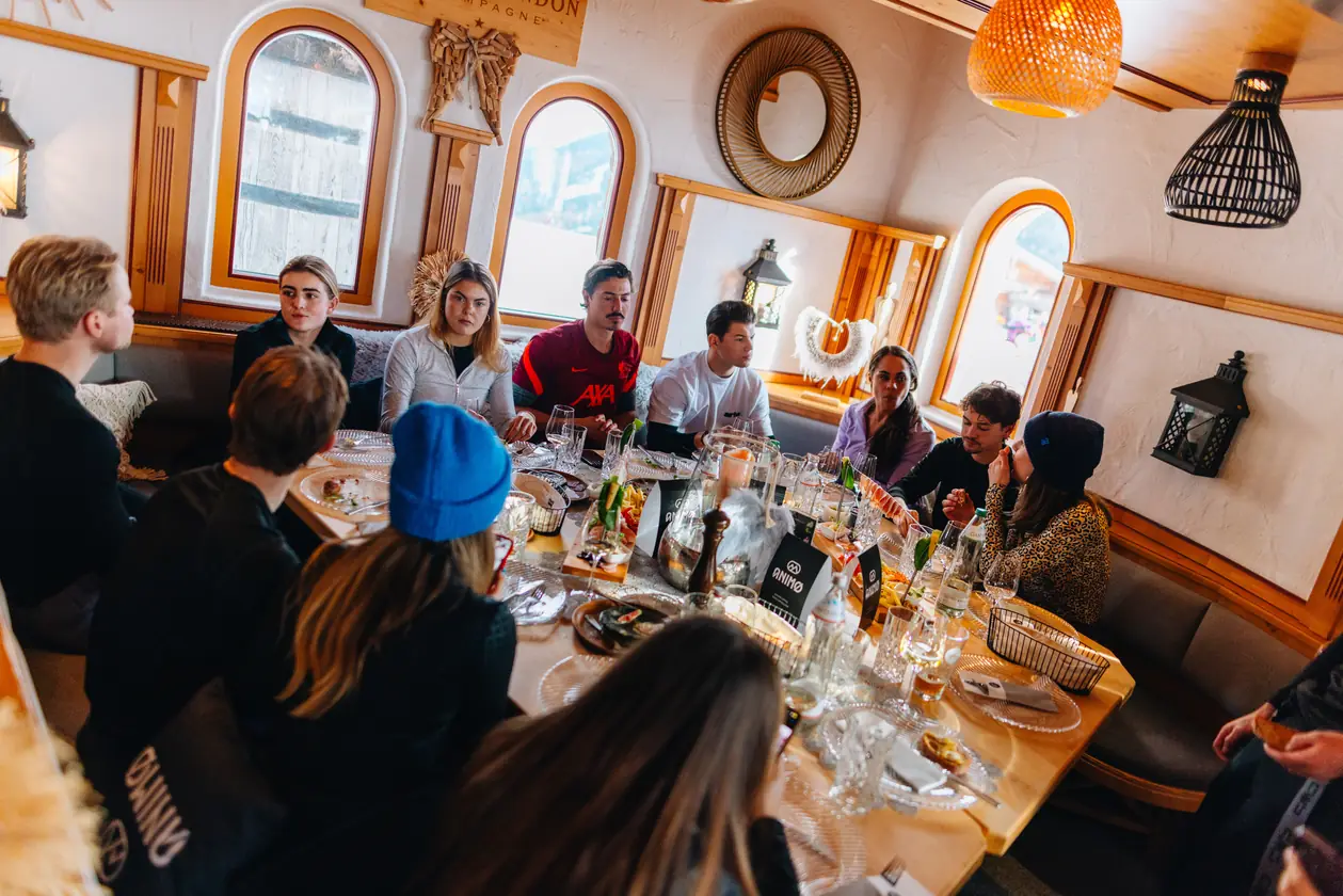 Een groep aan een lange tafel in een houten berghut.