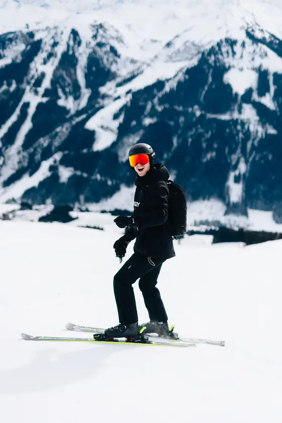 Een skiër in zwarte jas op de piste, met besneeuwde bergen op de achtergrond.