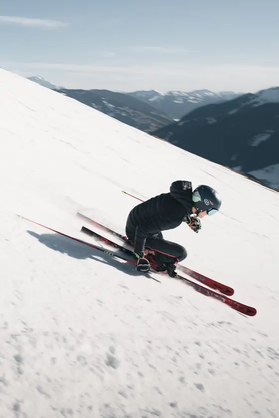 Een skiër snijdt door de sneeuw op een steile, zonnige helling.