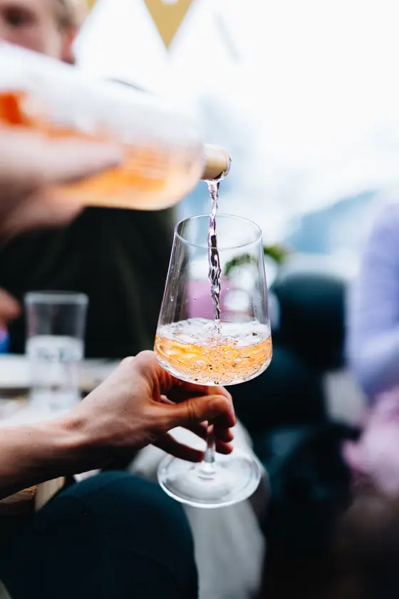 Een hand schenkt een oranje aperitief in een wijnglas.