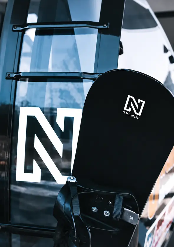 Een zwart snowboard met het N-logo, in beeld voor een raam.