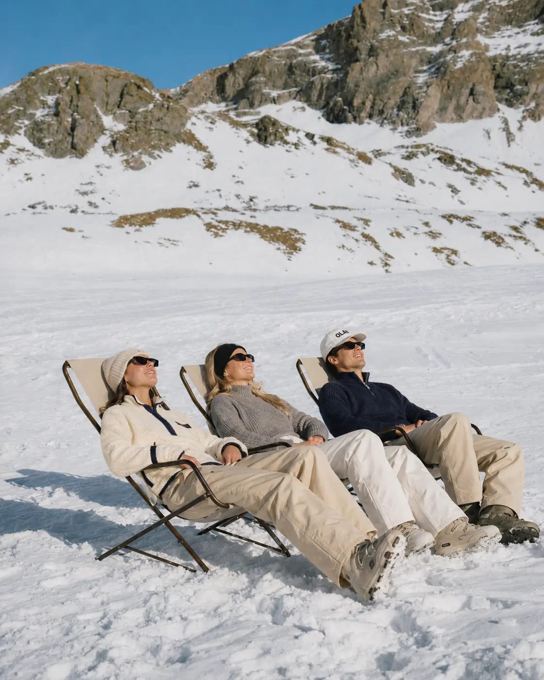 Twee mensen languit in ligstoelen in de sneeuw, met een besneeuwd bergdal achter zich.