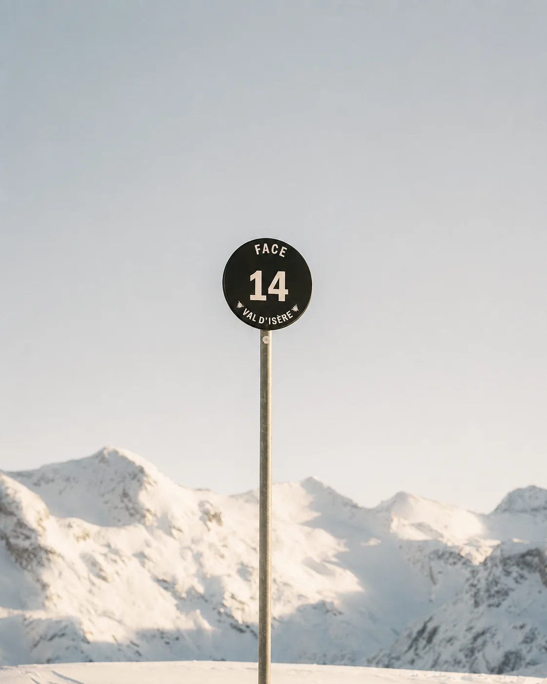 Een rond pistebord met het nummer 14 tegen een lege lucht, met besneeuwde toppen eronder.
