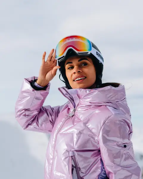Een vrouw met roze skihelm en een metallic lila jas in de sneeuw.