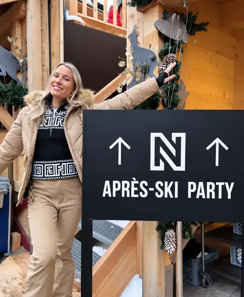 Een blonde vrouw in beige skikleding bij een branded après-skibord.
