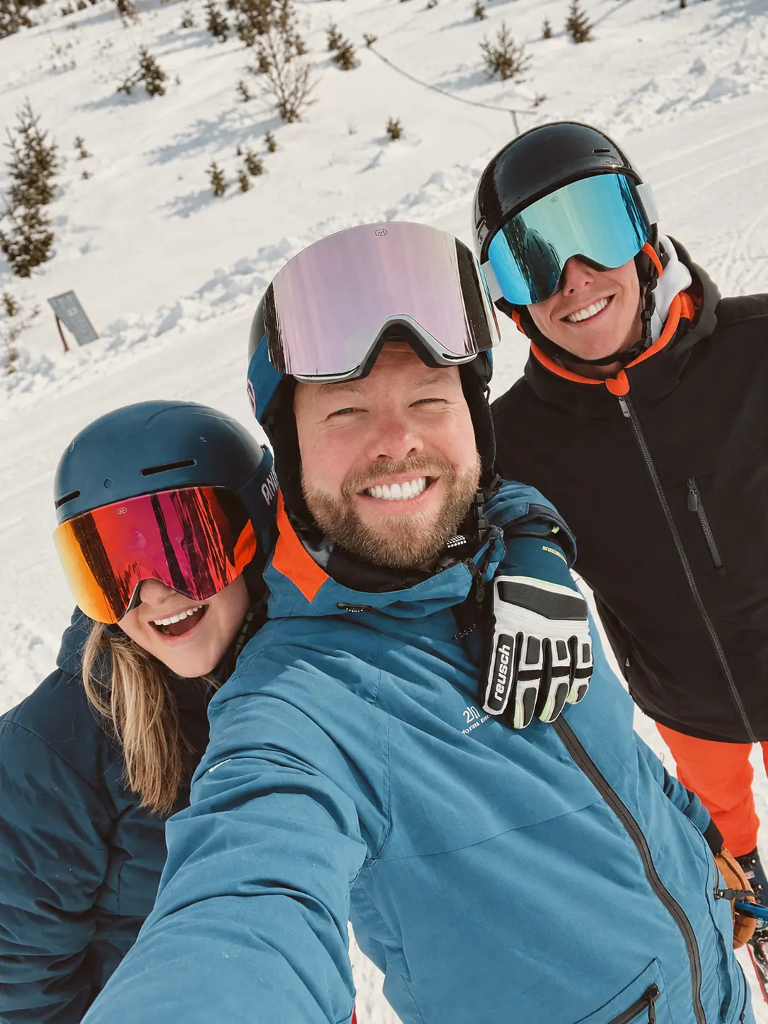 Het team van Altitude: drie lachende skiërs met helm en skibril maken een selfie op de piste.