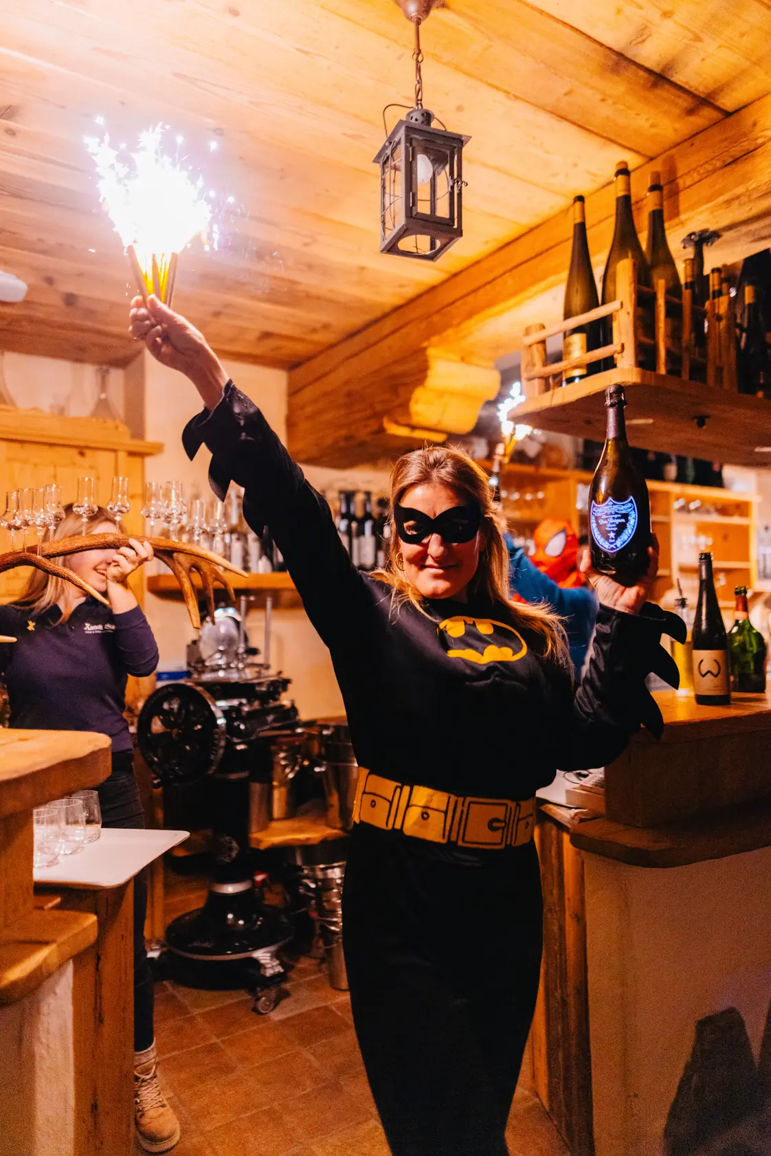 Een vrouw in een Batgirl-pak met een sterretje en een fles champagne in een houten berghut.
